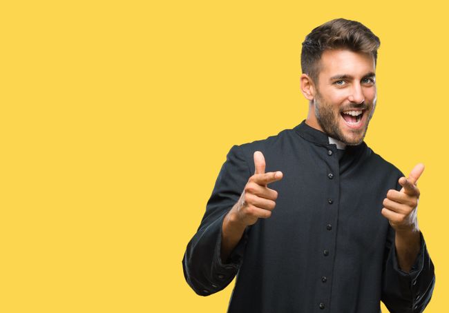 Young catholic christian priest man over isolated background pointing fingers to camera with happy and funny face. Good energy and vibes.