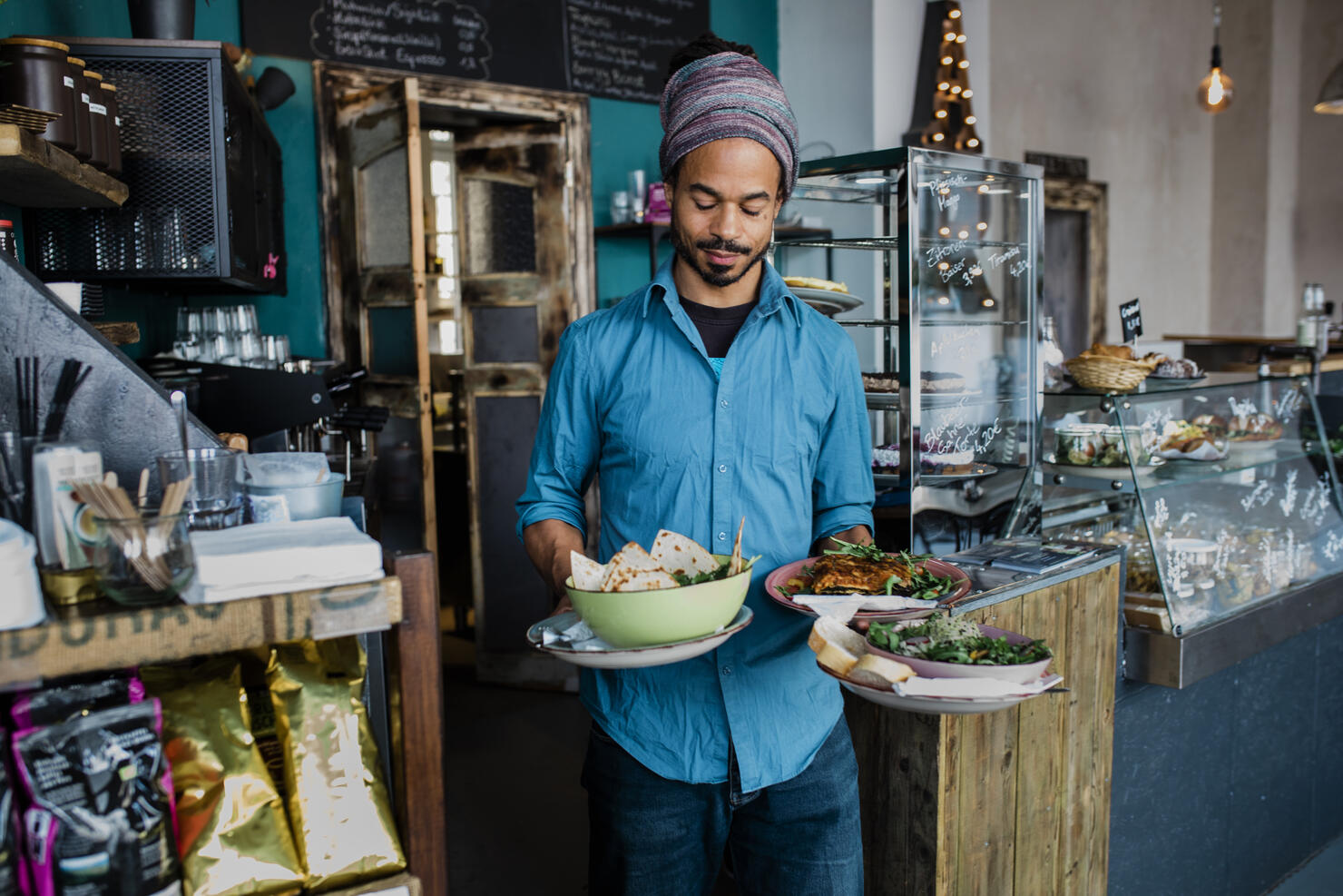 Waiter Carrying Bowls Of Food To Customers In Cafe