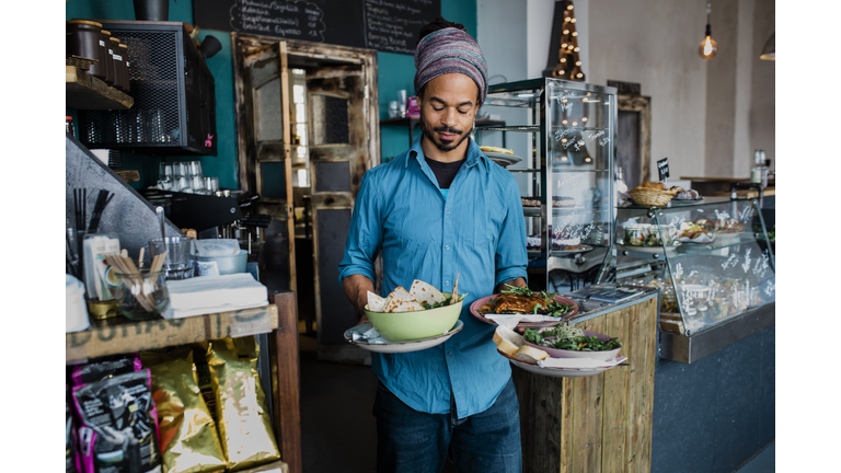 Waiter Carrying Bowls Of Food To Customers In Cafe