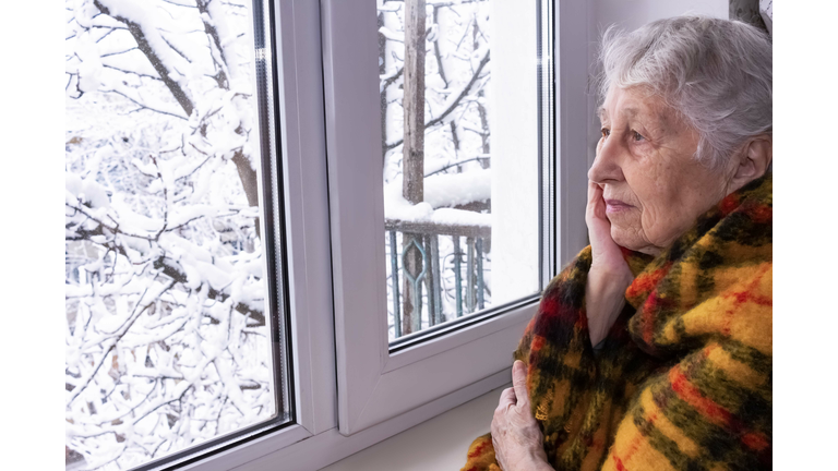 Old lonely woman sitting near the window in his house.