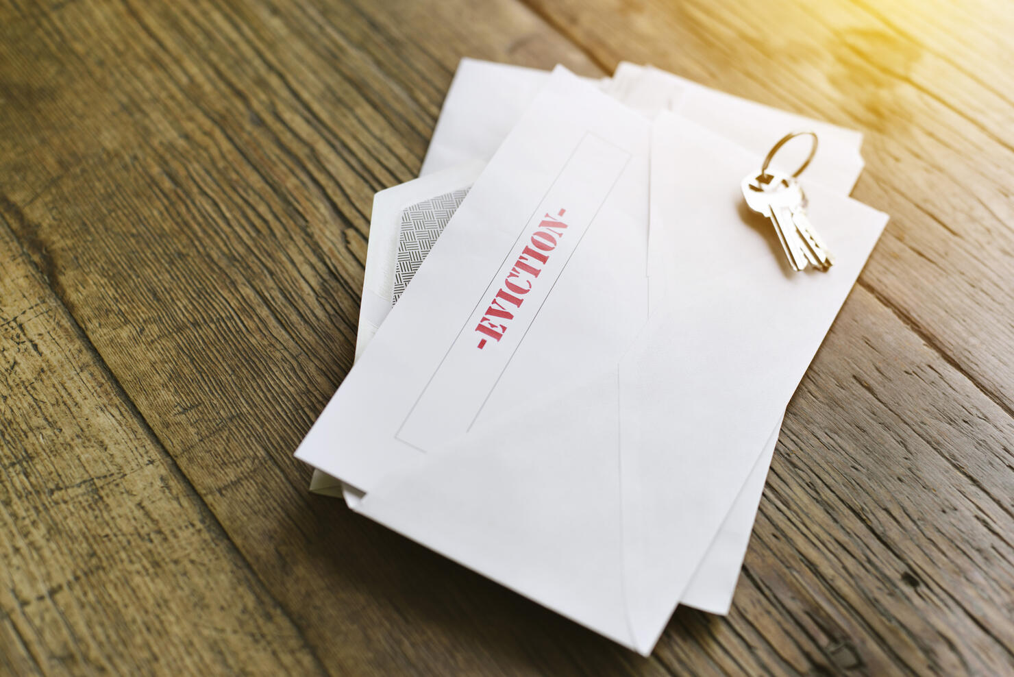 Notice of Eviction Opened in an Envelope with House Keys on a Wood Table - Sun shining through - Late Rent - Mortgage