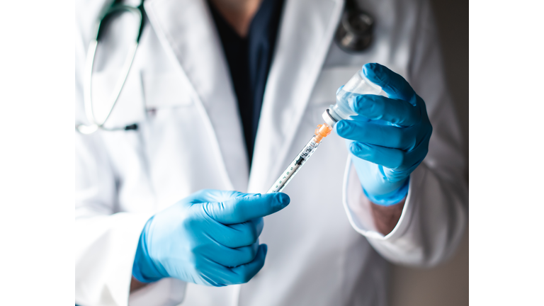 Doctor in white coat drawing vaccine into a syringe for injection.