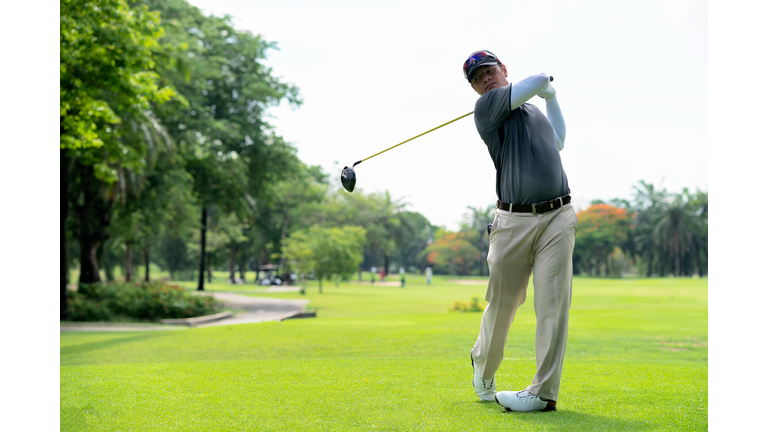 Golfer hitting golf shot with club on course while on summer vacation. Golfer swings his driver off the tee.