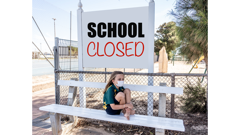 Covid-19 outbreak schools closures. Sad and bored Schoolgirl kid with face mask feeling depressed and lonely outside her closed school. Restrictions and lockdown as Coronavirus containment measures.