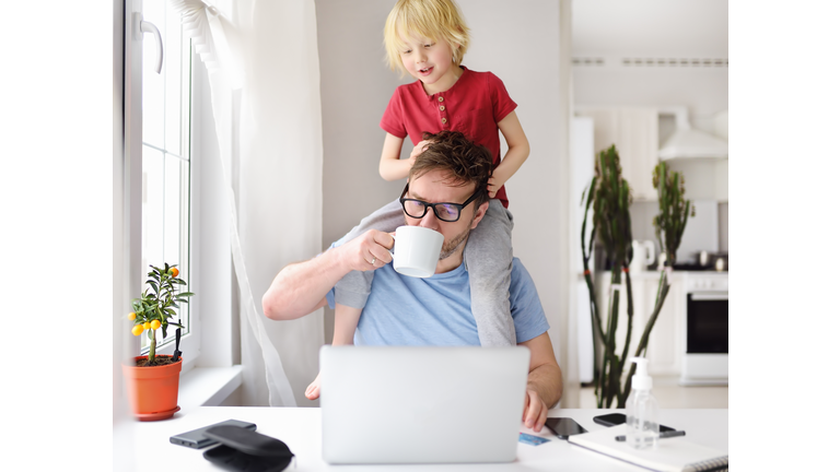 Man working from home with laptop during quarantine. Home office and parenthood at same time. Exhausted parent with hyperactive child.