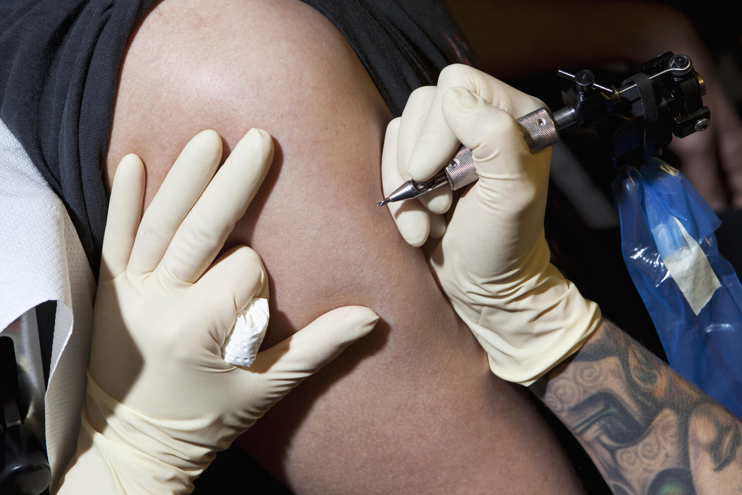 A tattoo artist preparing to tattoo a man's bare arm, close-up