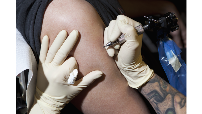 A tattoo artist preparing to tattoo a man's bare arm, close-up