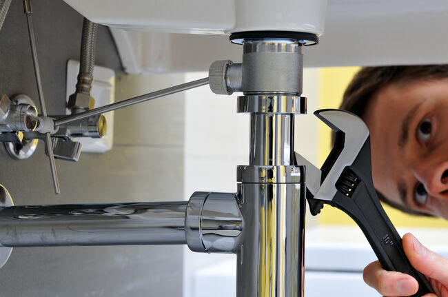 Close-up of plumber with wrench doing repairing work