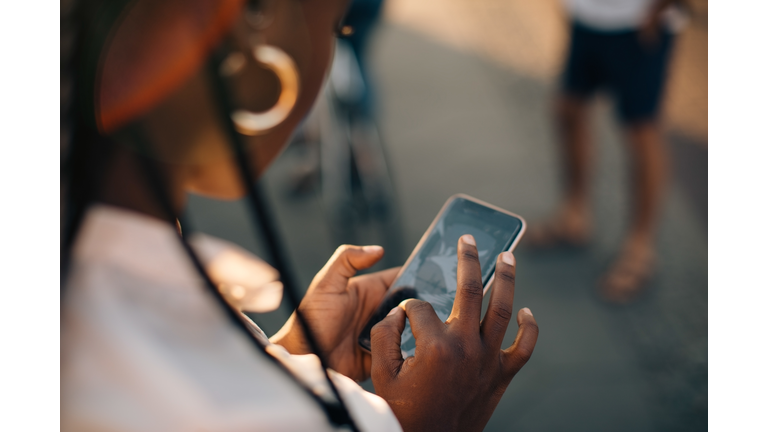 Cropped image of young woman using smart phone while standing on street in city