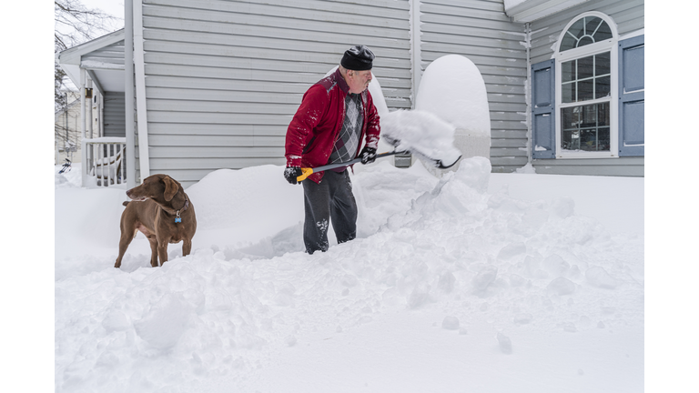 Man cleaning the snow after a snowfall around his house, making a way to propane tanks with his dog
