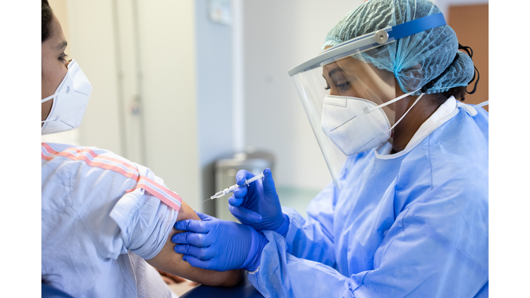 Doctor in personal protective equipment vaccinating a patient