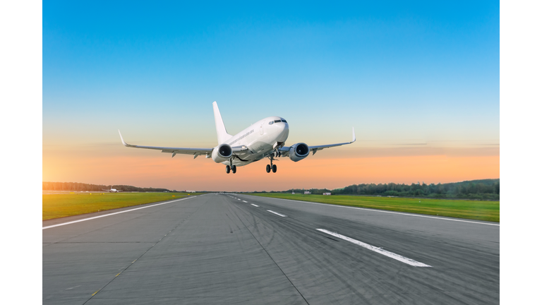 Passenger plane fly up over take off runway from airport at sunset.