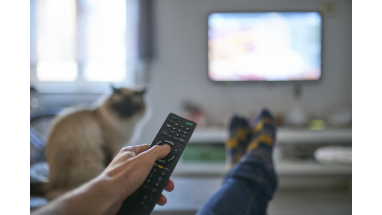 Hand of man pointing remote control at working television screen