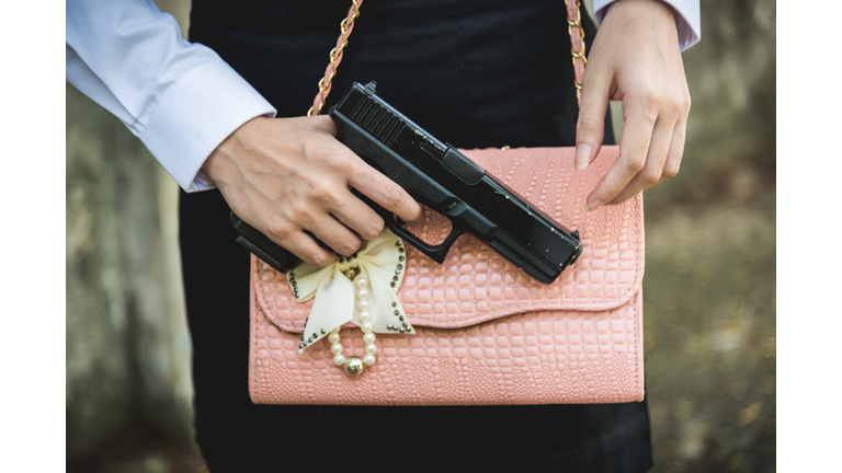 Midsection Of Woman With Shoulder Bag Holding Gun