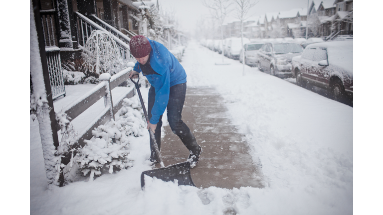 A man shovels the sidewalk outside of his suburban house.