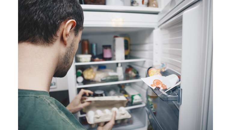 Man holding egg carton by refrigerator in kitchen
