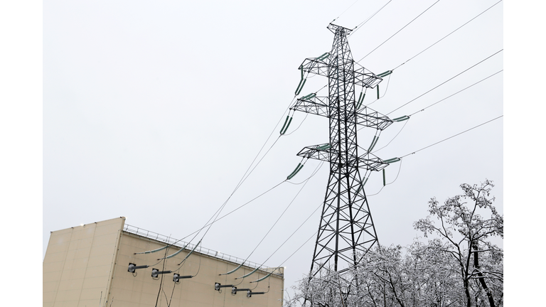 High voltage tower with electrical wires and the building of electric substation on winter sky background