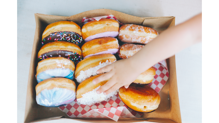 Cropped Hand Touching Donuts In Box