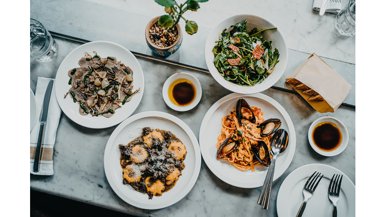 Flat lay of meal for two people with fresh green salad, appetizer, seafood linguine and beef ravioli freshly served on dining table in a restaurant