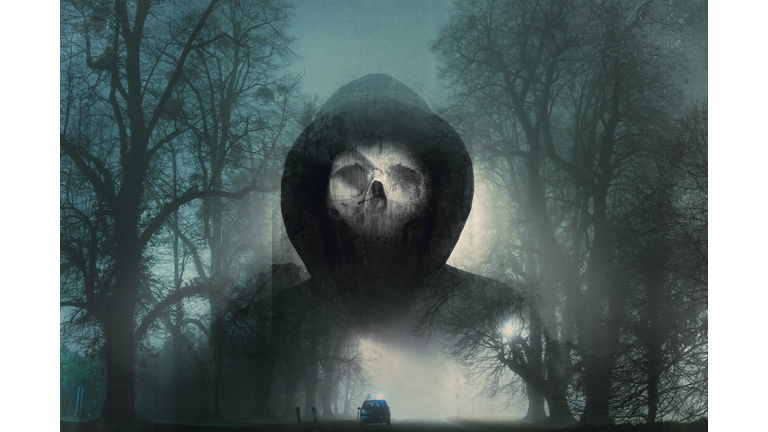 A double exposure of a scary hooded figure with a skull for a face. Over layered with a misty road on a winters night. With a blurred, grunge, vintage, abstract edit
