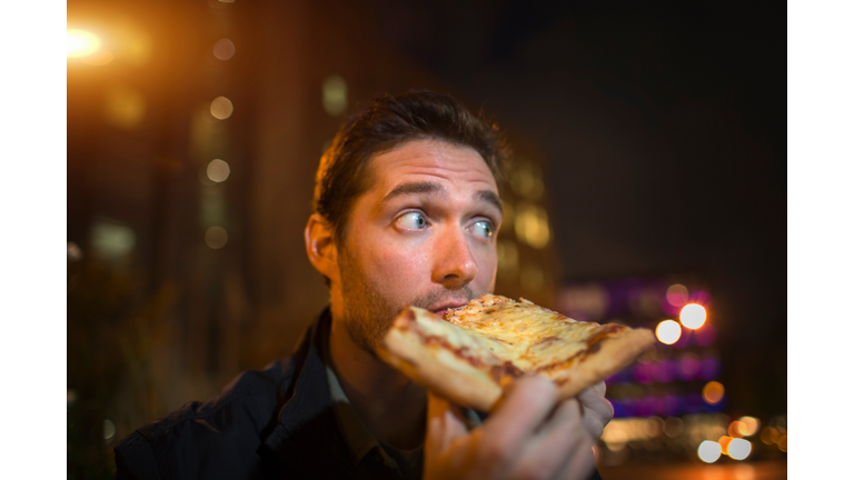 Man eating pizza on city street