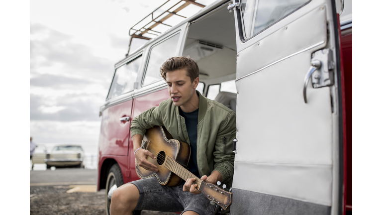 Young man playing guitar at a van