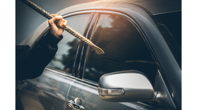 A robber dressed in black holding crowbar at a driver in a car. Car thief concept.