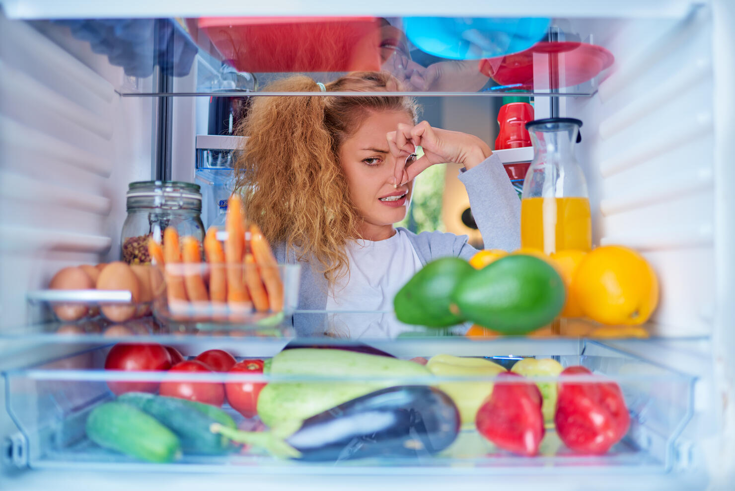 Woman standing in front of opened fridge and holding up to her nose.