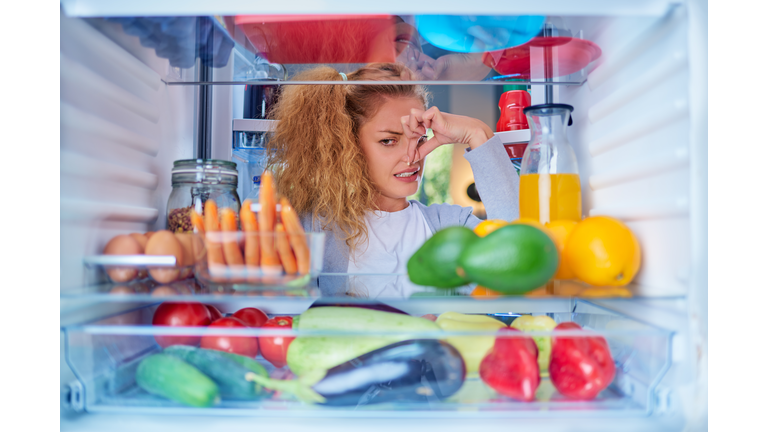 Woman standing in front of opened fridge and holding up to her nose.