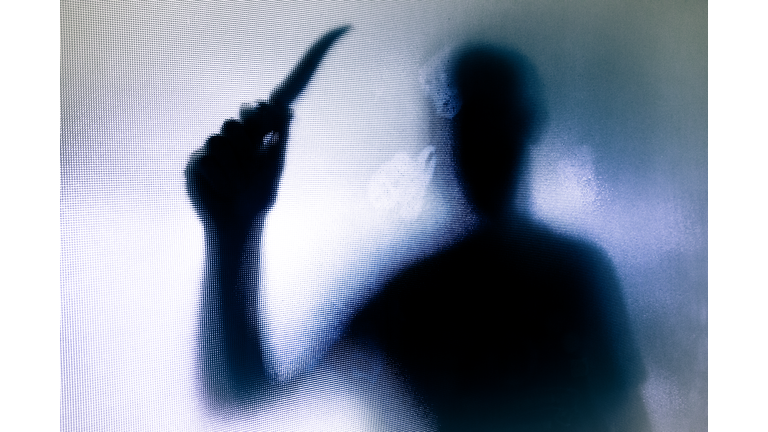 Violent threatening silhouette of man wielding a knife behind frosted glass window