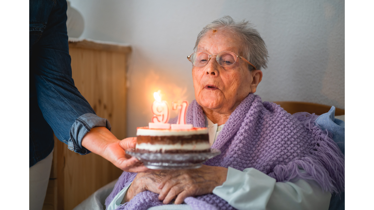 Old woman blows the candles from his 96th birthday cake with daughter