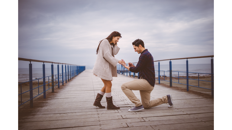 Man on one knee proposing to girlfriend on a pier