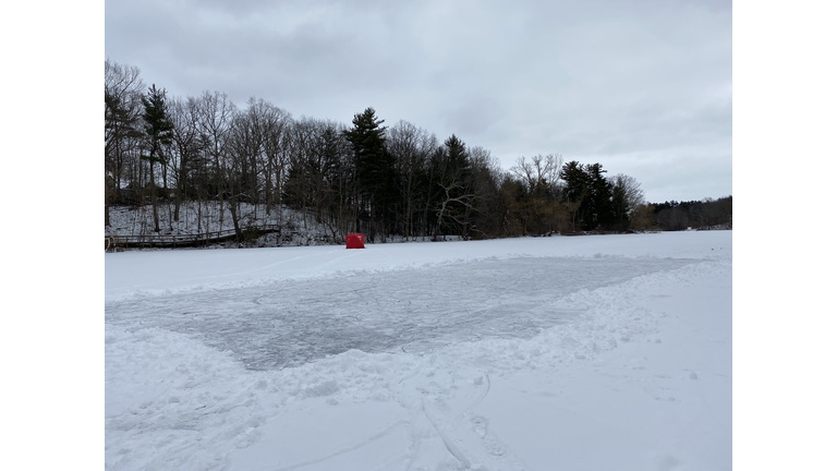 Red ice fishing tent behind pond hockey rink on frozen pond. Wintertime activity in Dorechester, Canada