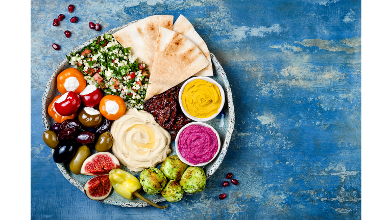 Middle Eastern meze platter with green falafel, pita, sun dried tomatoes, pumpkin and beet hummus, olives, stuffed peppers, tabbouleh, figs. Mediterranean appetizer party idea