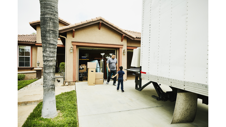 Young son helping father move items from moving truck into new house