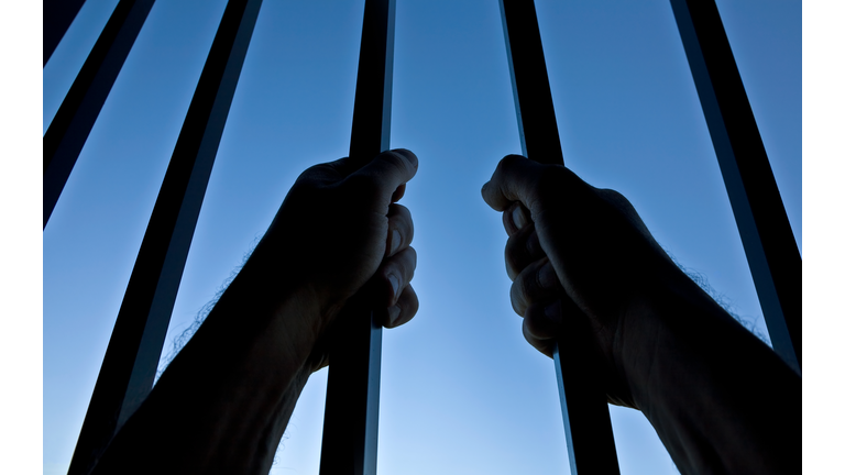 Silhouette of Hands Behind Jail Bars Against Clear Blue Sky