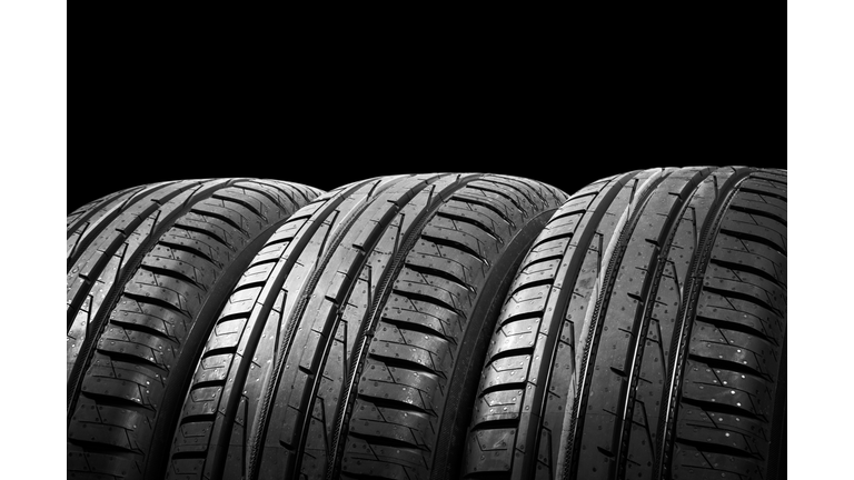 Studio shot of a set of summer car tires isolated on black background. Tire stack background. Car tyre protector close up. Black rubber tire. Brand new car tires. Close up black tyre profile. Car tires in a row
