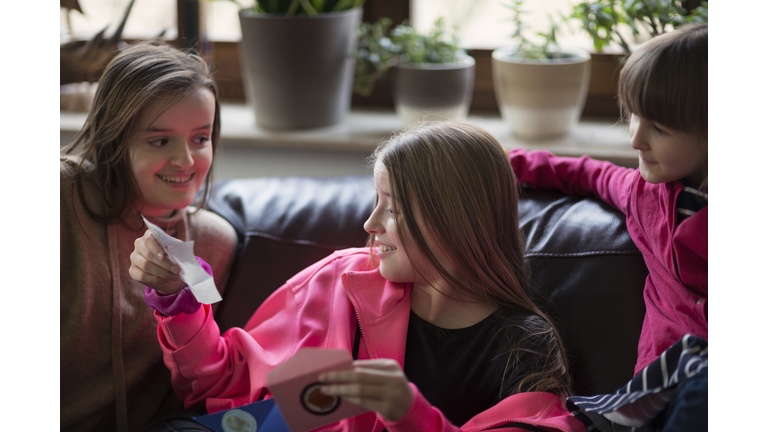 Surprised teenager opening a birthday gift voucher from her two sisters