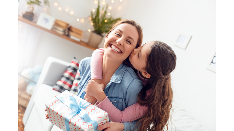 Mother and daughter at home mother's day sitting daughter hugging mom kissing cheek joyful