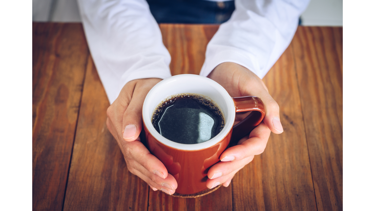 Someone hands holding a mug of black coffee before drinking.