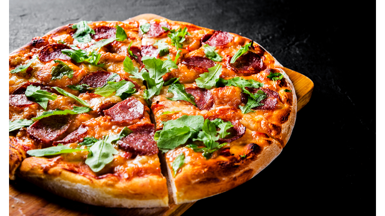 Pepperoni Pizza with Mozzarella cheese, salami, Tomato sauce, pepper, Spices and Fresh arugula. Italian pizza on Dark grey black slate background