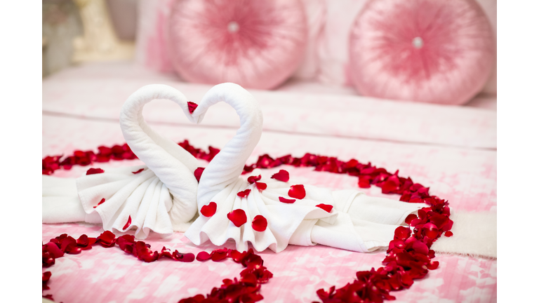 two swans made from towels are kissing on honeymoon white bed.