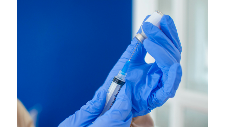 A young doctor in blue protective glove is holding a medical syringe and vial