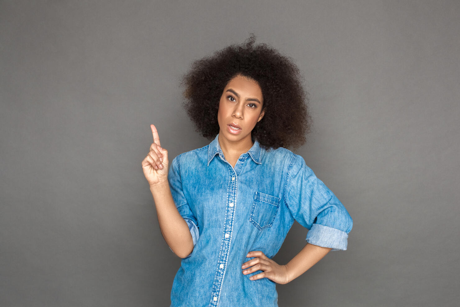 Freestyle. woman standing isolated on grey pointing up looking camera sassy