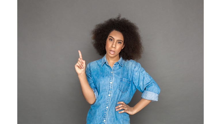 Freestyle. woman standing isolated on grey pointing up looking camera sassy