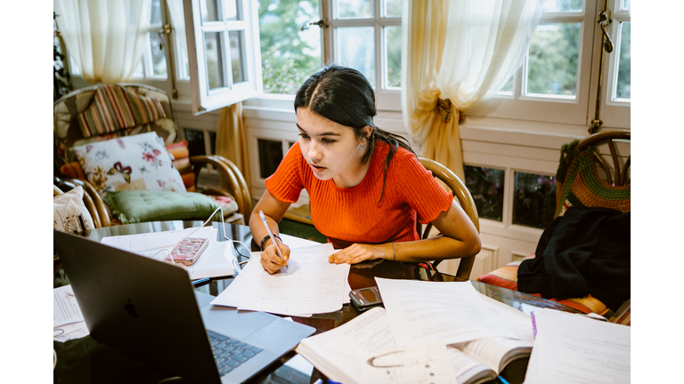 hispanic college student doing some home works from home with laptop