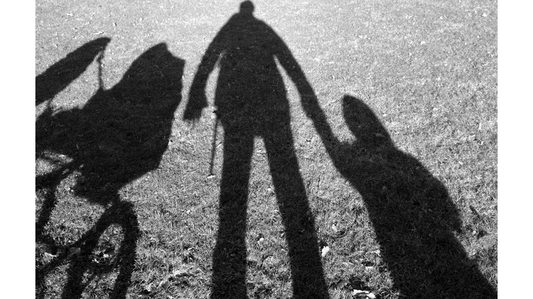 Shadows of person holding hands with a baby and a stroller