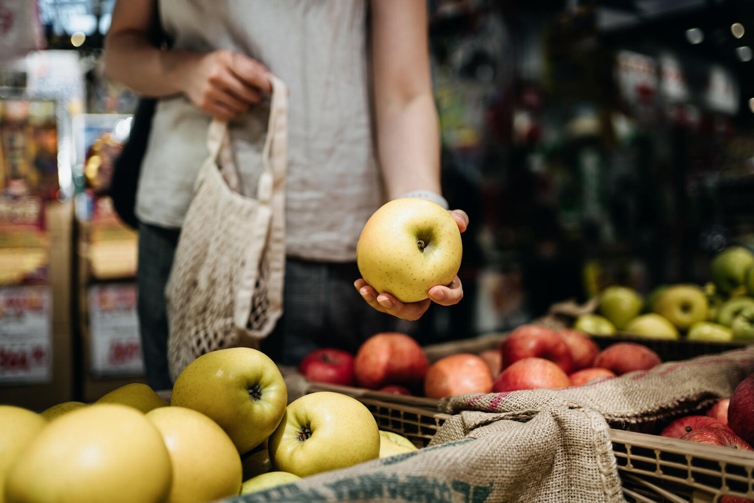 Close up of young Asian woman shopping for fresh organic fruits in farmer's market with a cotton mesh eco bag. Environmentally friendly and zero waste concept