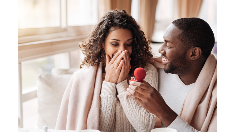 Amazed African American couple getting engaged in the cafe