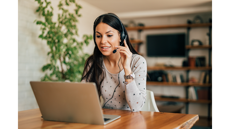 Portrait of a cute woman with headset and laptop at home office.